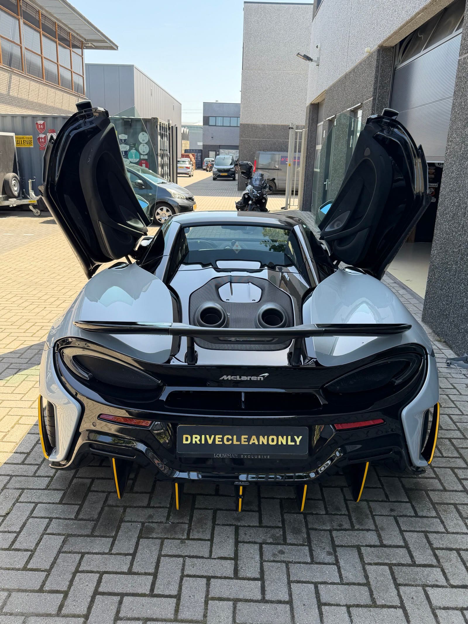 Zilvergrijze McLaren met geopende vleugeldeuren en DriveCleanOnly-kentekenplaat na een detailbehandeling